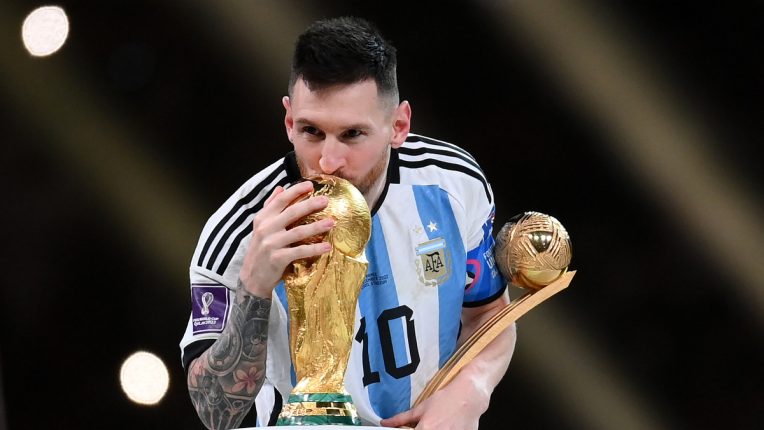 Lionel Messi kicks the World Cup while holding the Golden Ball trophy
