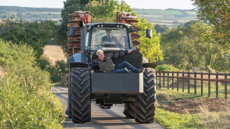 Jeremy Clarkson riding a tractor, with Kaleb hitching a ride, in Clarkson's Farm season 2